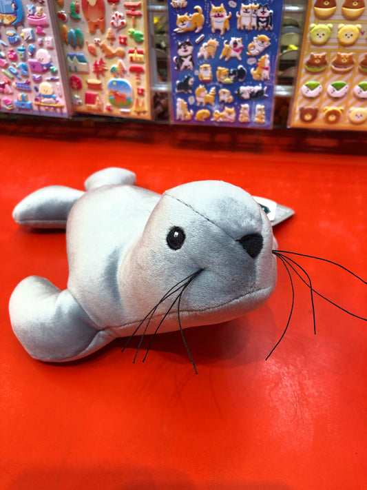Soft gray Mary Meyer Smootheez seal plush toy on red surface, with colorful sticker sheets in background