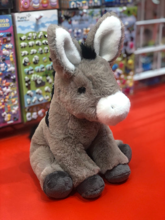 Soft gray donkey plush toy with large ears sitting on red surface, surrounded by colorful toy displays in background