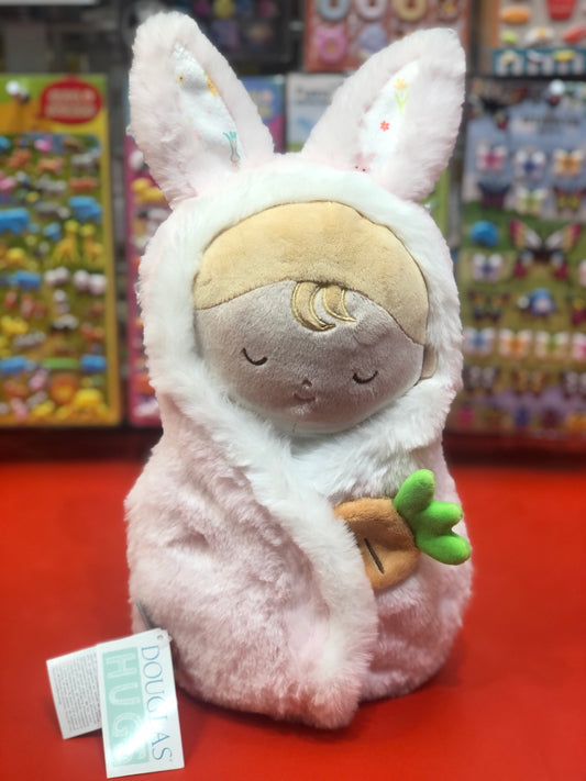 Soft pink Douglas Baby Bunny Hug plush toy with embroidered face, bunny ears, and carrot detail, displayed in toy store