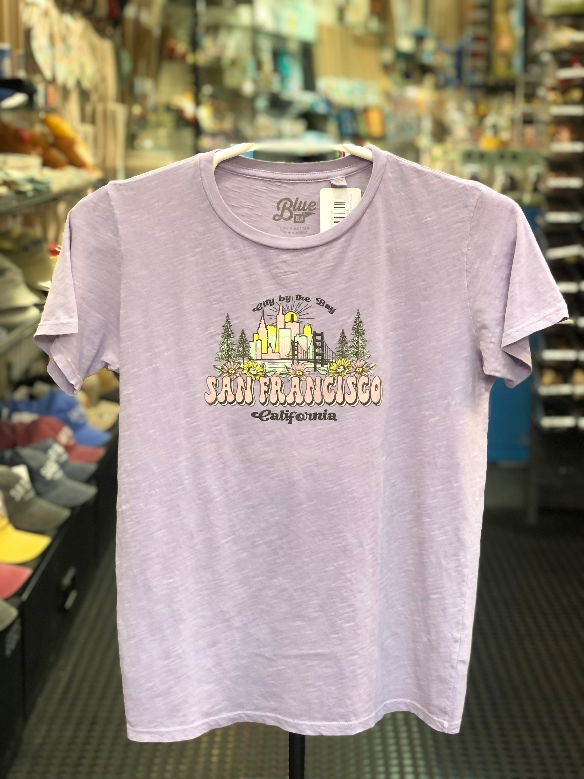 Lake Shirts light purple t-shirt with 'San Francisco California' design on a hanger in a store setting.