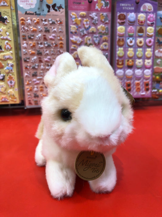 Soft, white Aurora Miyoni Tots baby bunny plush on red surface with colorful sticker sheets in background