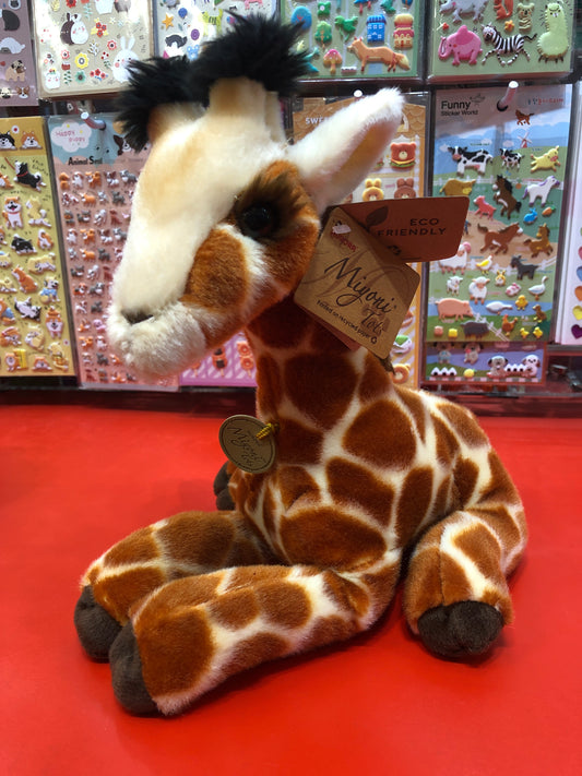 Cuddly Aurora Miyoni Tots Giraffe Calf plush toy with realistic markings, displayed on red surface against colorful animal sticker background
