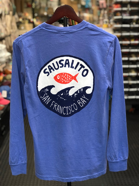Back view of a flo blue garment-dyed long-sleeve t-shirt on a hanger, featuring a large circular graphic inspired by traditional Japanese woodblock prints with a bright red fish leaping over deep blue and white ocean waves under bold text reading "SAUSALITO SAN FRANCISCO BAY".