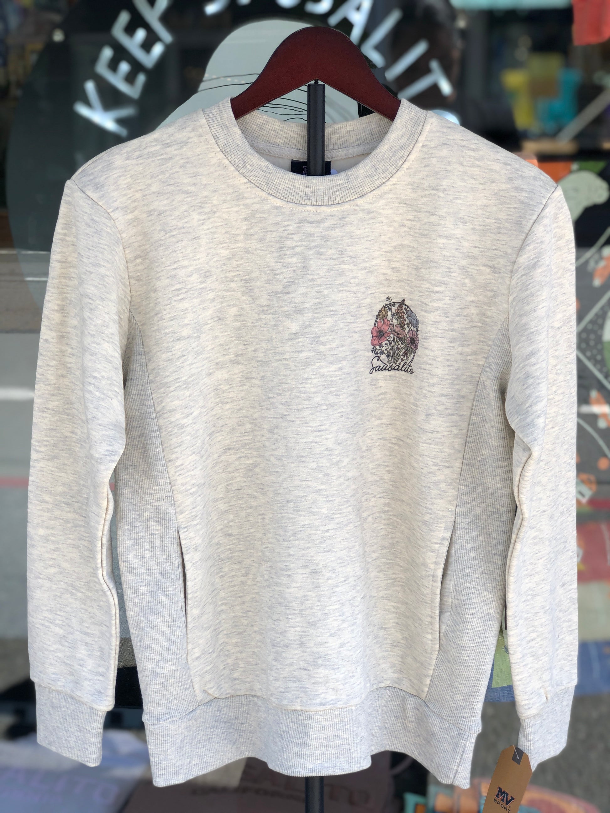 Oatmeal-colored women's fleece sweater with pockets featuring a floral crest on the front chest