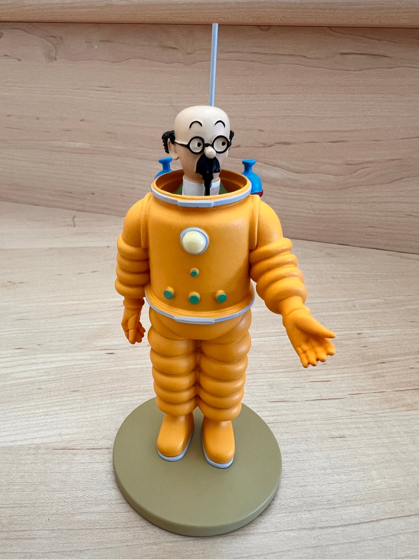 Front view of a hand-painted 12cm Professor Calculus resin figurine wearing a detailed orange moon spacesuit, standing on a round olive-green base against a light wood background.
