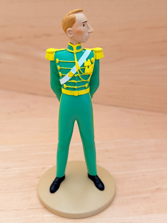 A 12 cm hand-painted resin figure representing the creator Hergé in a cameo appearance from the Tintin album King Ottokar’s Sceptre. The figure is depicted standing at attention in a bright green Syldavian full dress uniform with a yellow collar, gold epaulets, gold braided detailing across the chest, a light blue ceremonial sash, and black shoes.