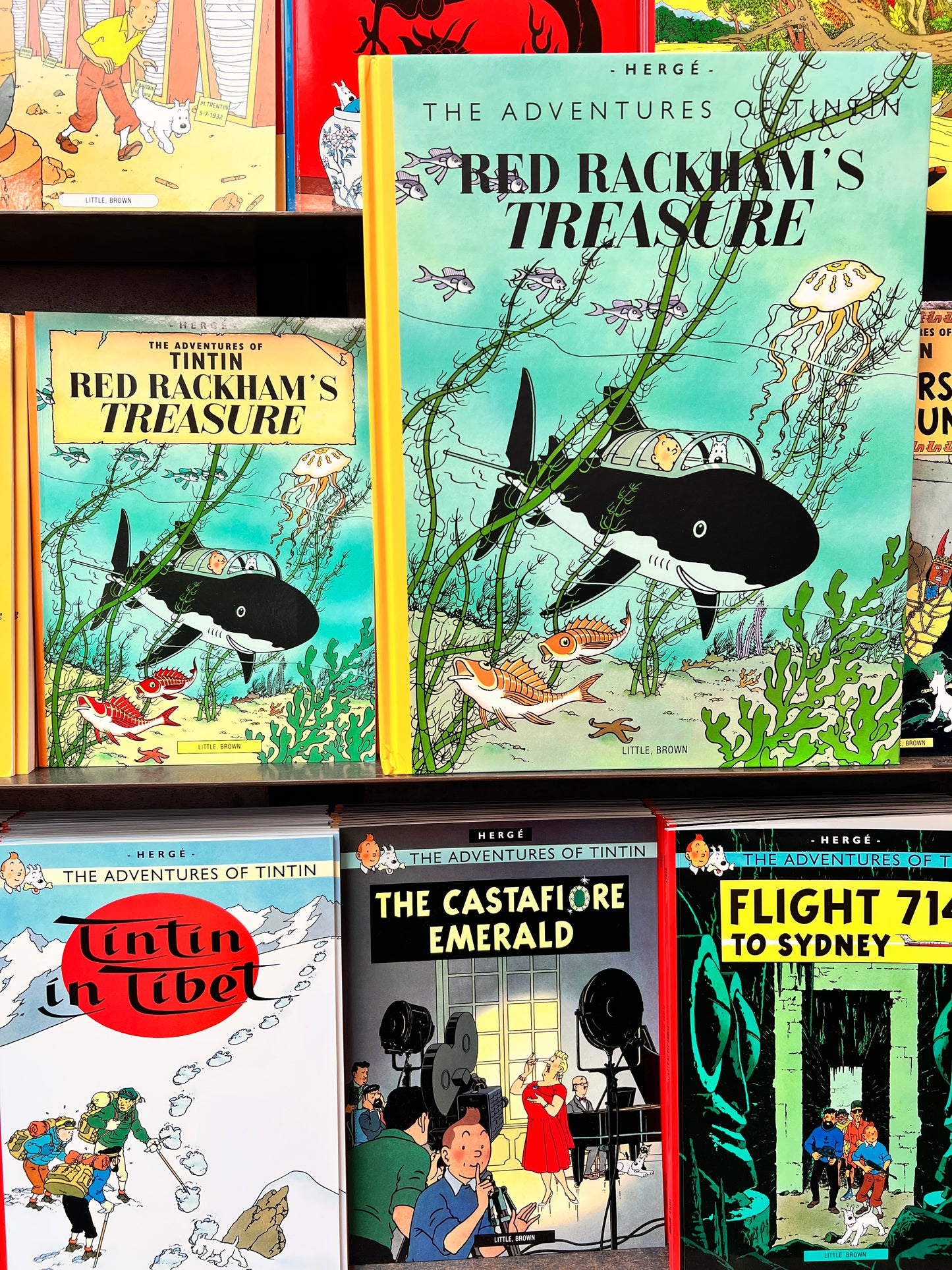 A side by side view showing the difference  of the 'Red Rackham's Treasure' large facsimile edition, demonstrating its oversized height compared to standard Tintin books on a display shelf.