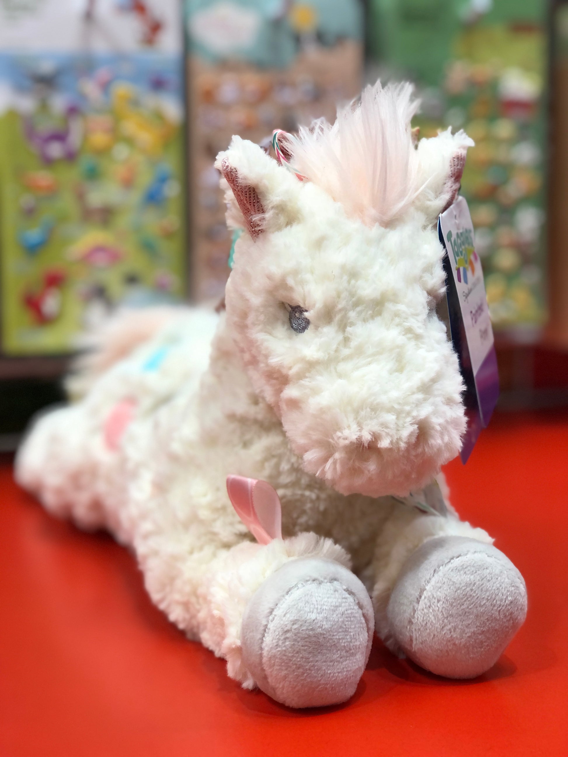 Plush unicorn toy with colofrul tags on a red surface