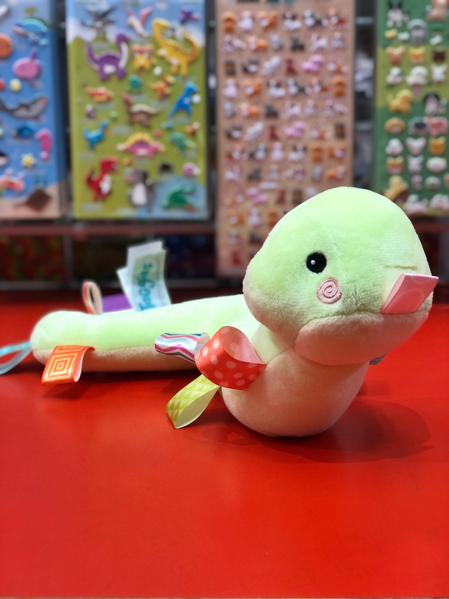 Plush toy resembling a green snake on a red surface with colorful stickers in the background