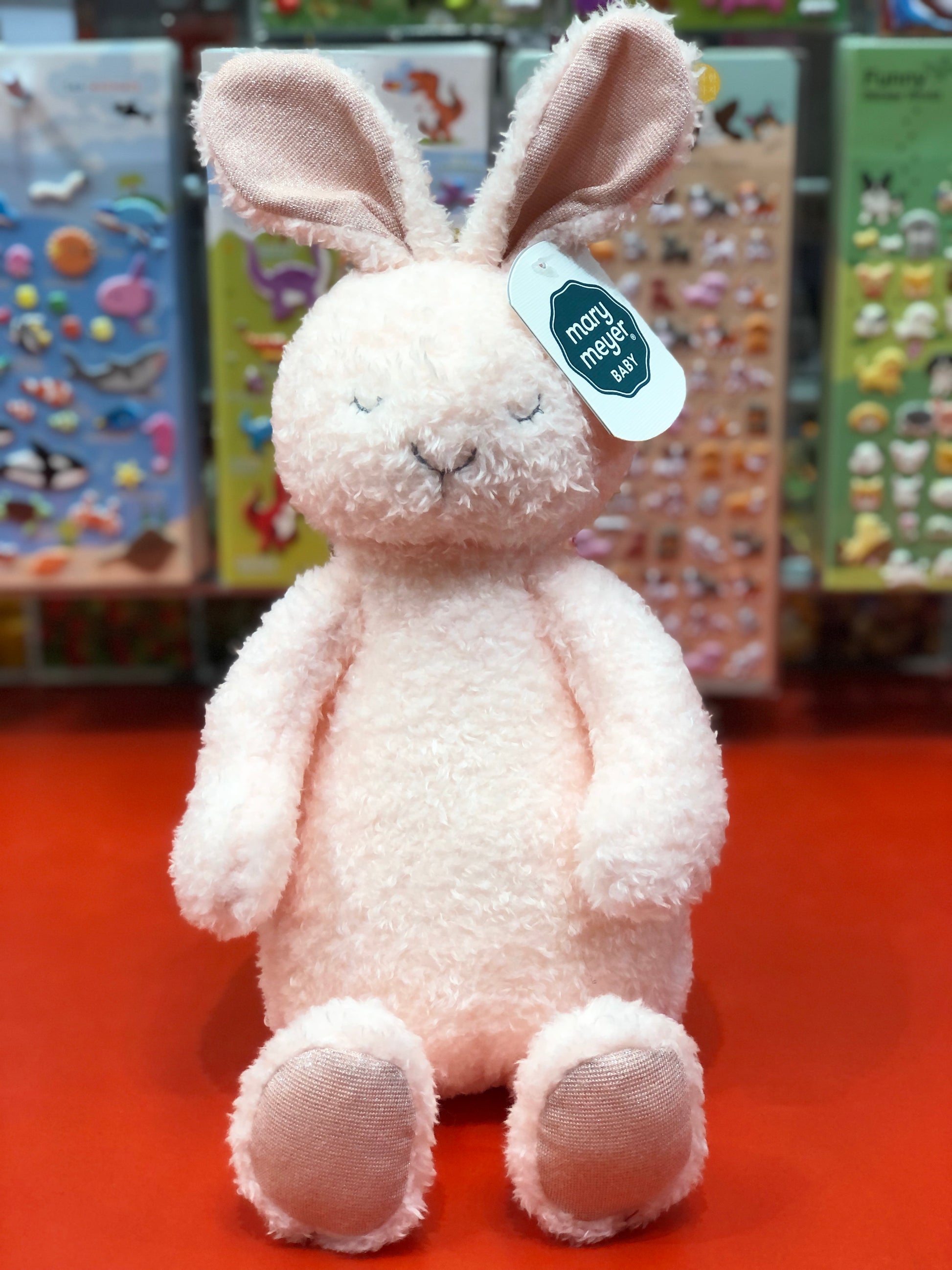 Pink plush bunny with a tag on a red surface with colorful background