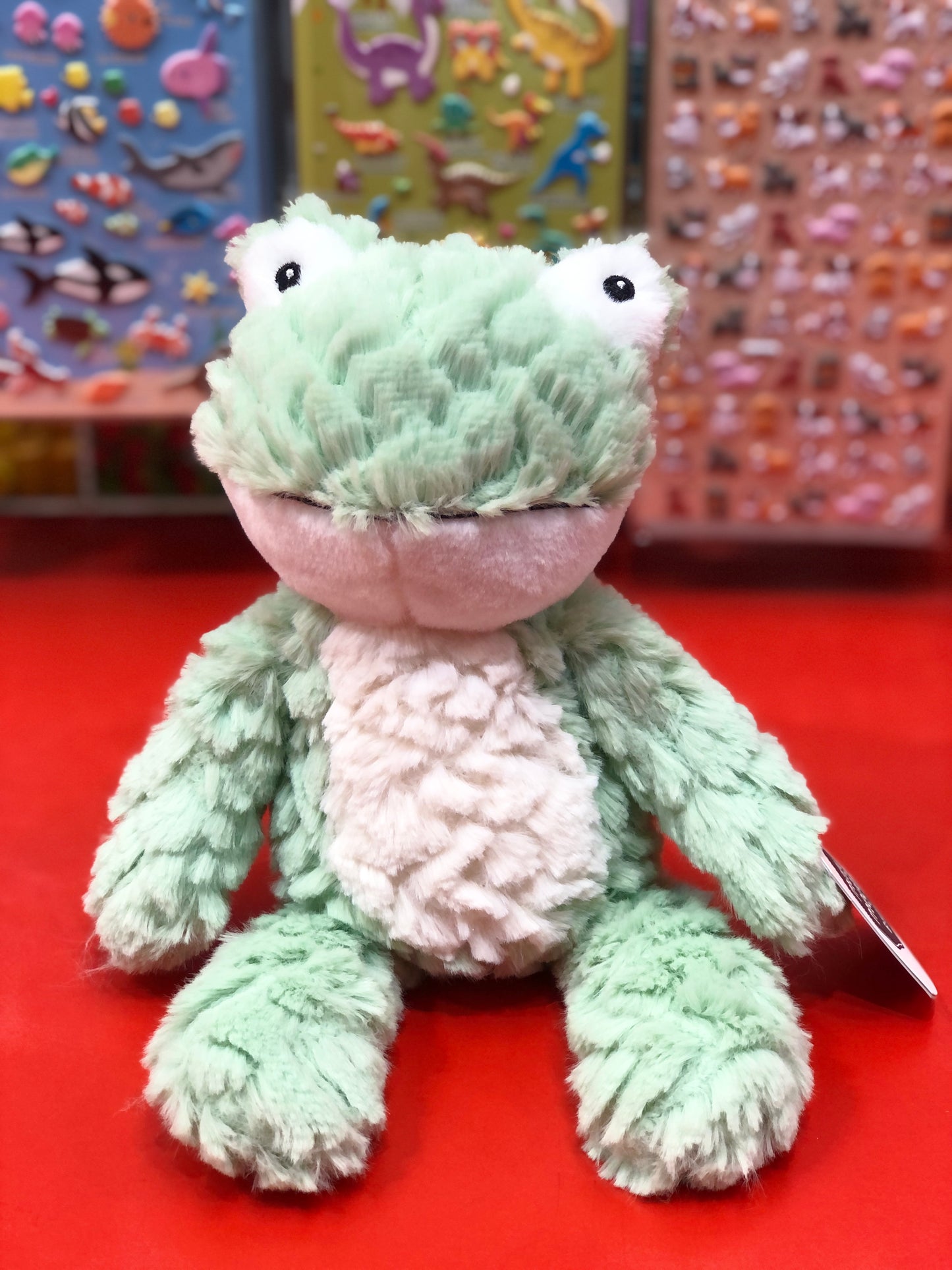 Plush frog toy on a red surface with colorful background