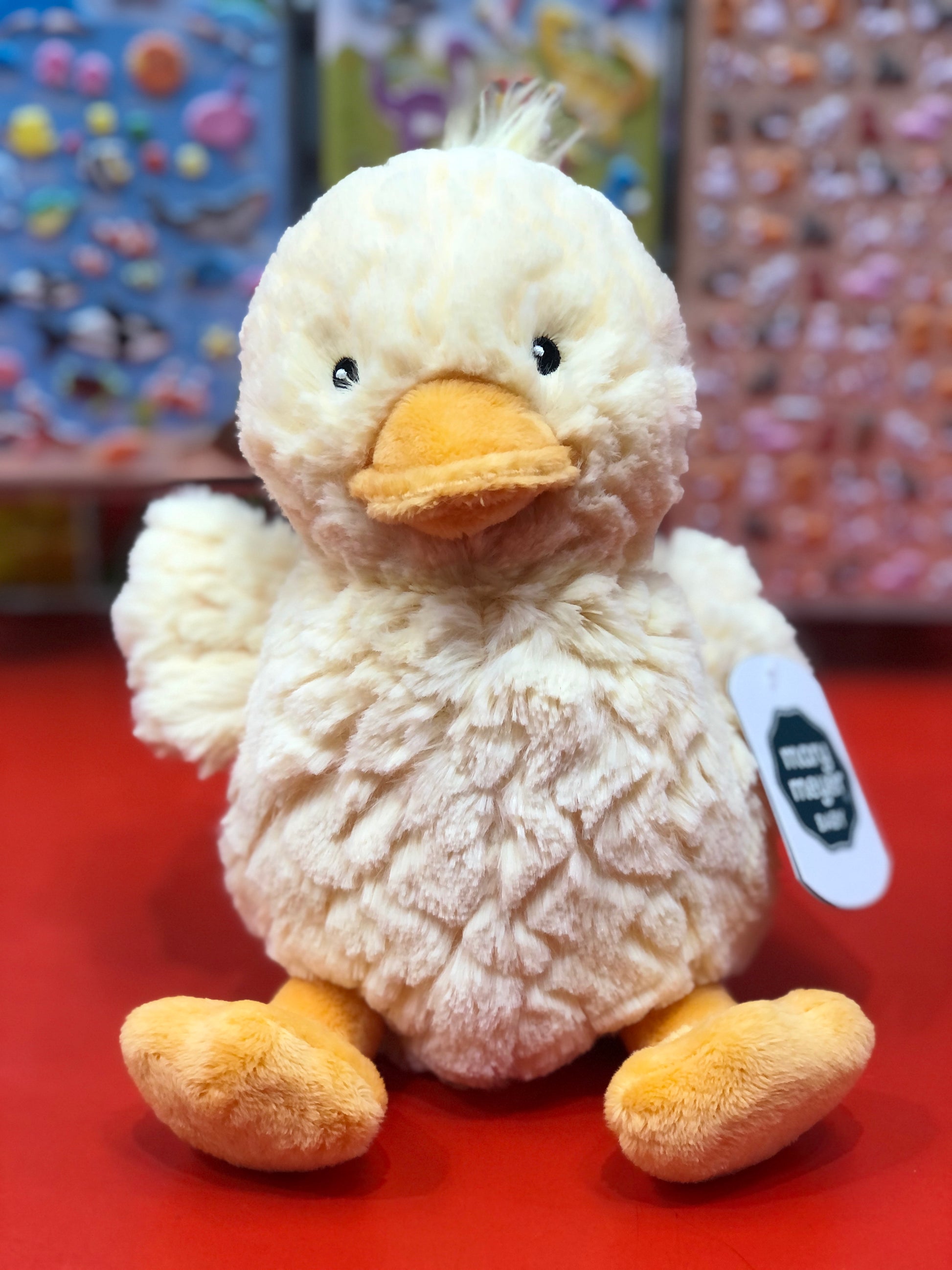 Plush duck toy with a tag on a red surface