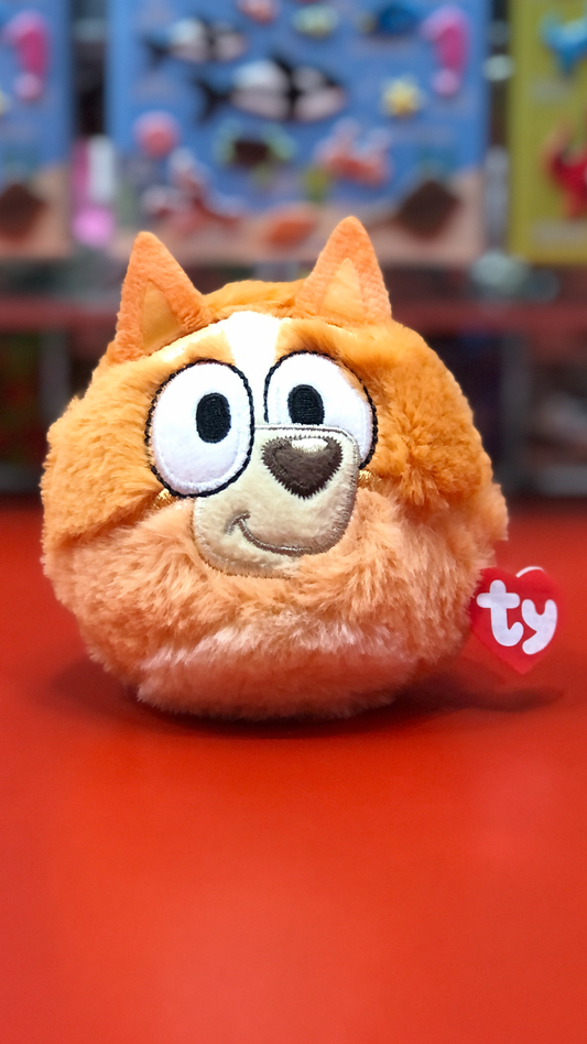 Orange plush toy with a smiling face on a red surface, featuring the Ty brand.