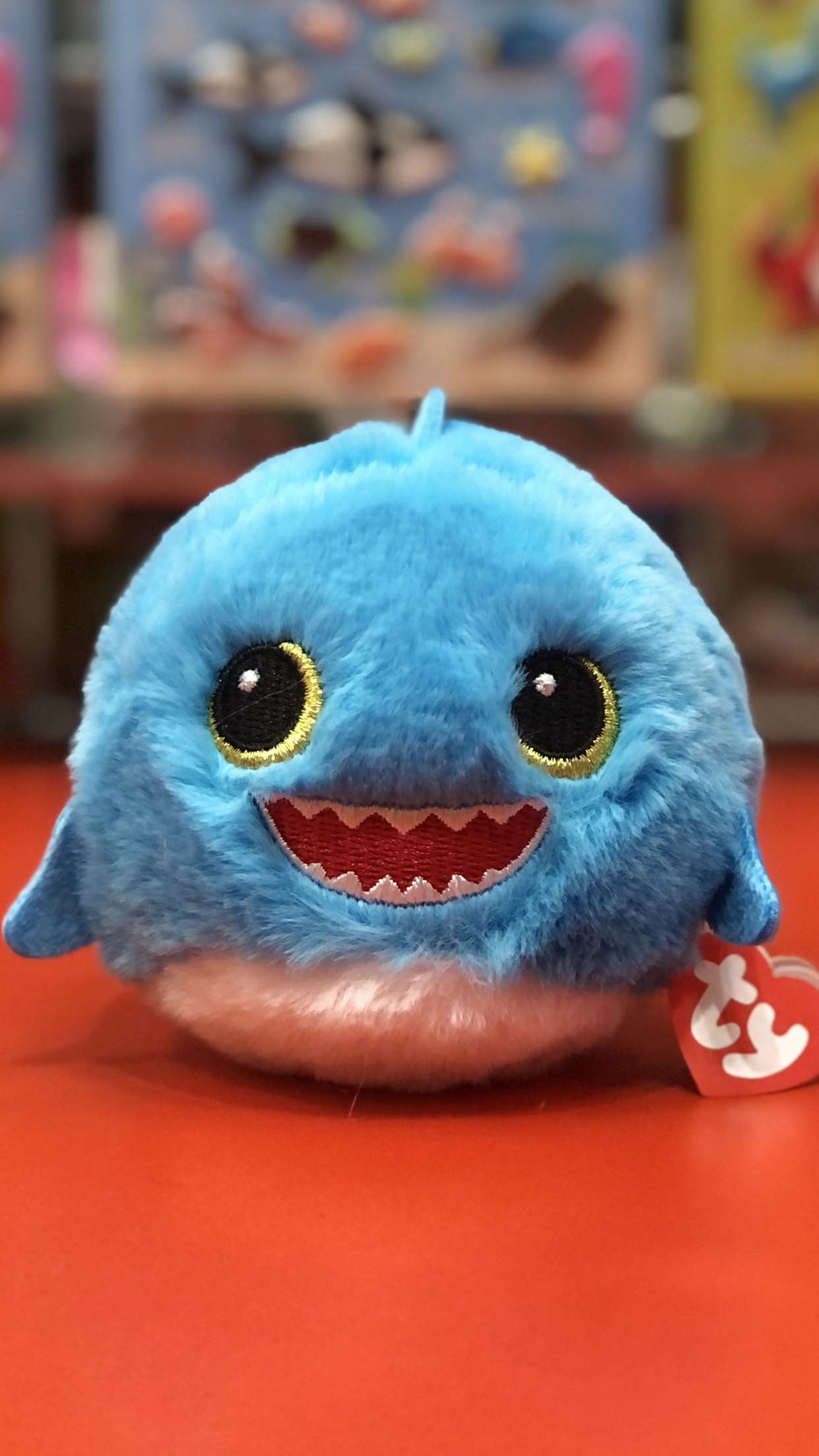 Blue Ty plush toy with a happy expression on a red surface