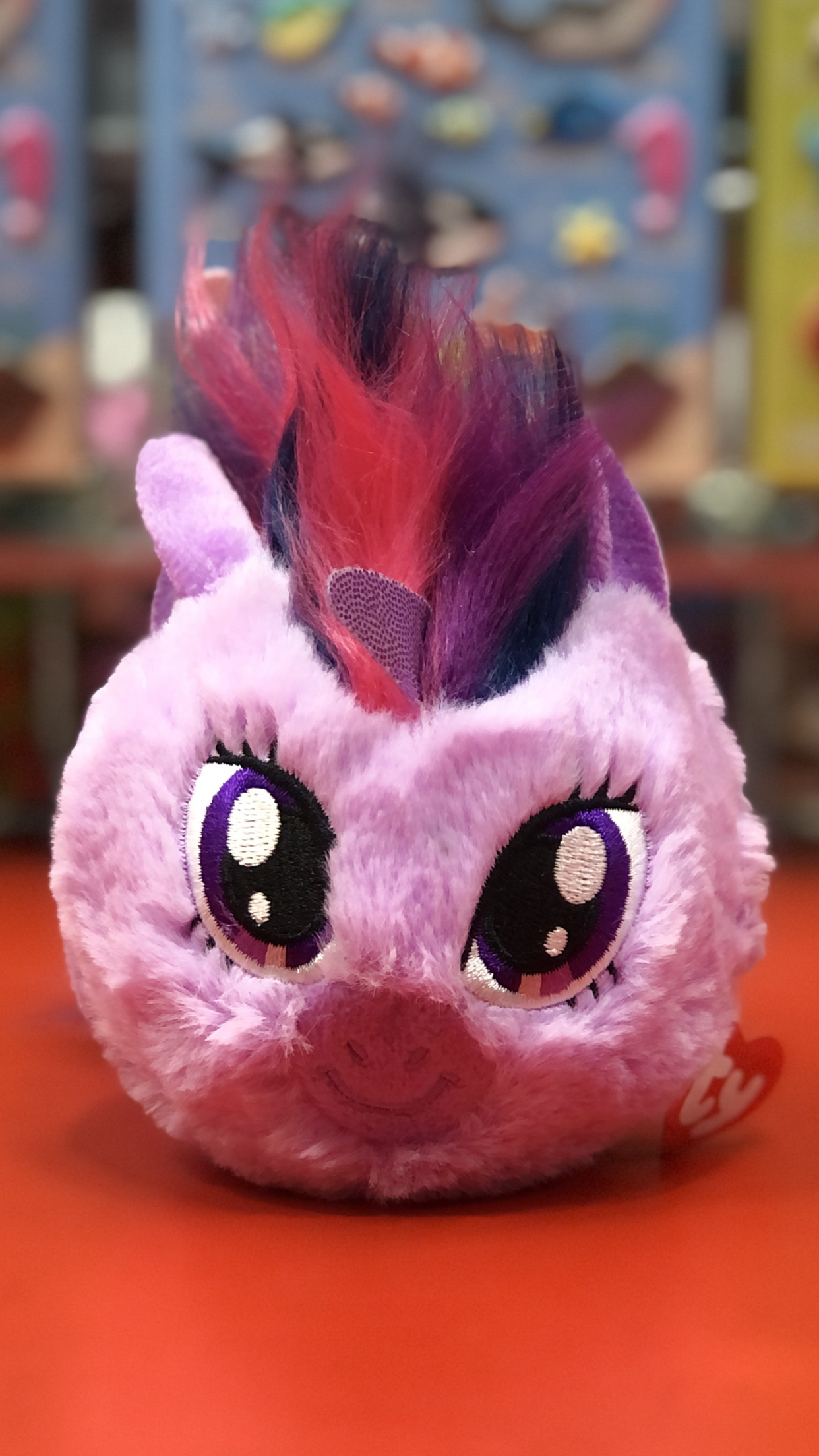 Pink Ty plush toy with purple and red hair on a colorful background.
