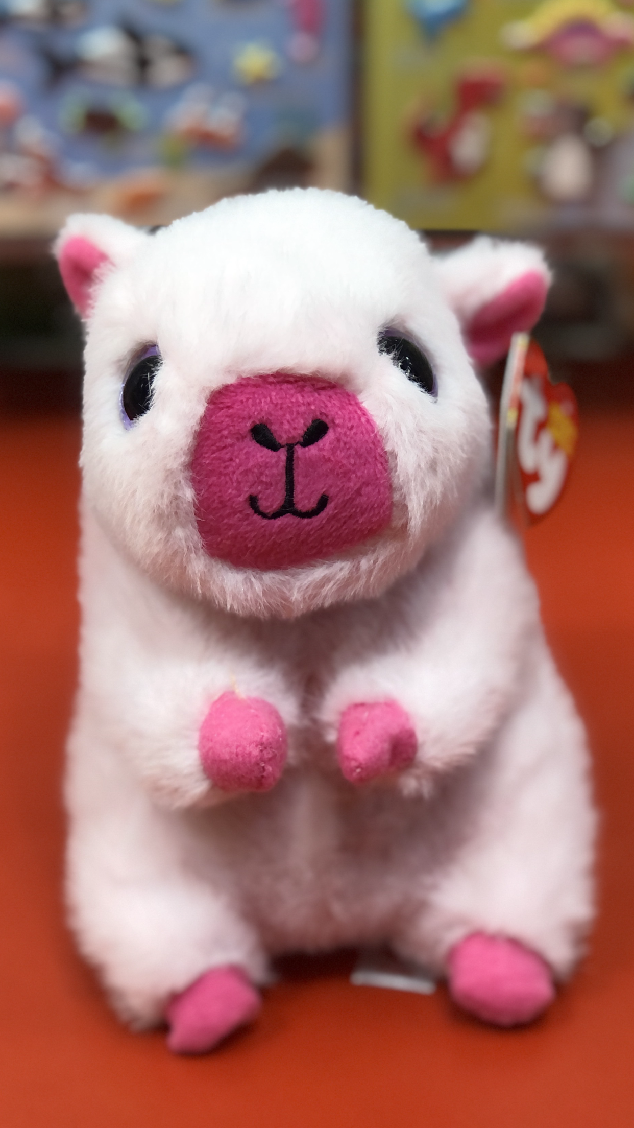 Smiling Ty pink capybara plush sitting on a red counter. 