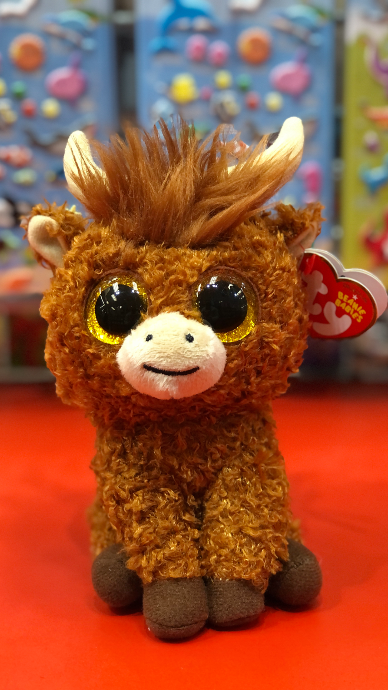 Ty brown highland cow plush toy with large gold glitter eyes on a red background. 