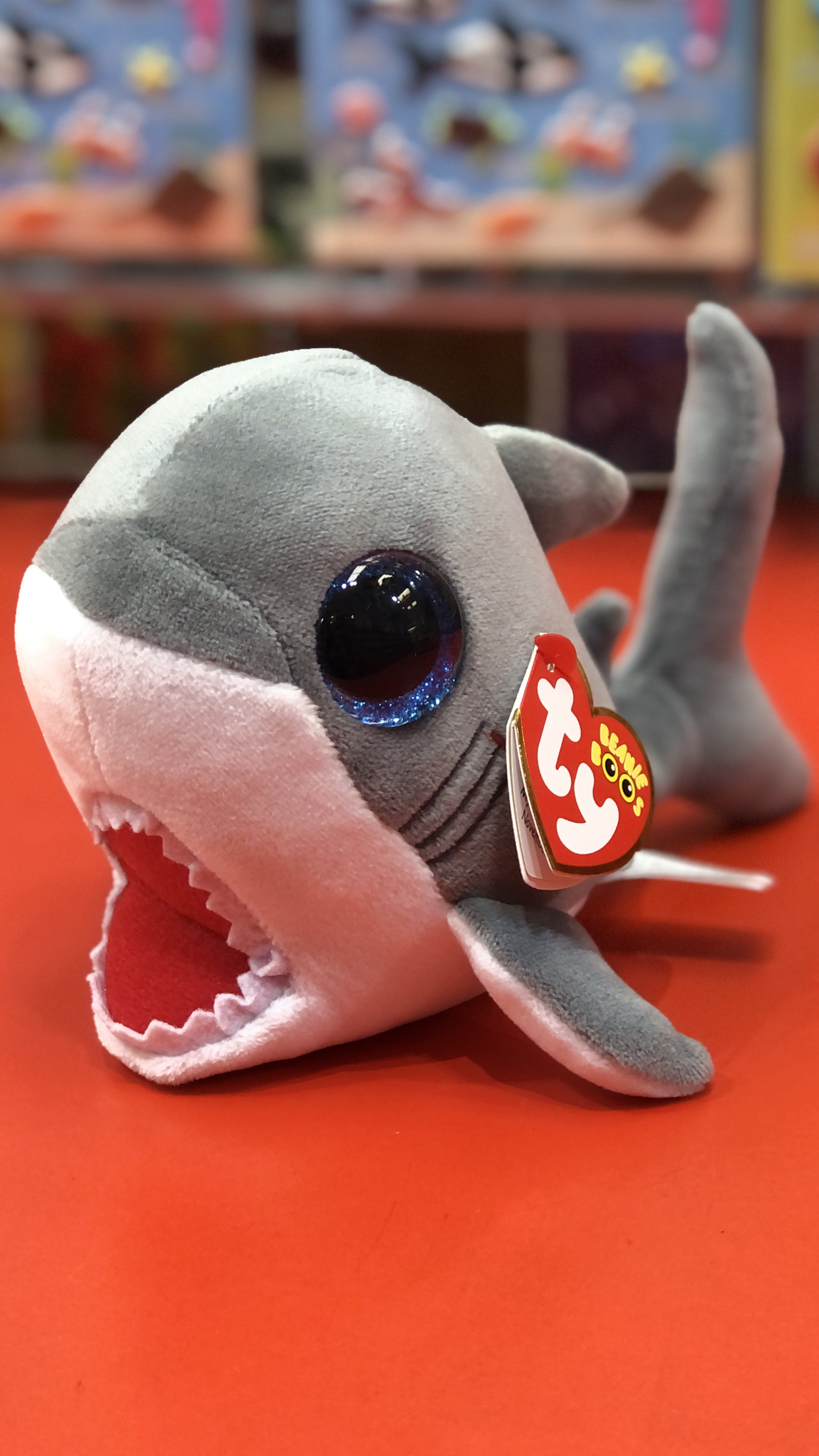 Ty great white shark plush with open jaws and blue glitter eyes on a red surface.