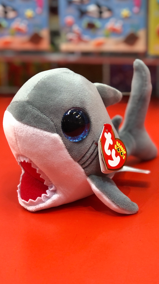 Ty great white shark plush with open jaws and blue glitter eyes on a red surface.