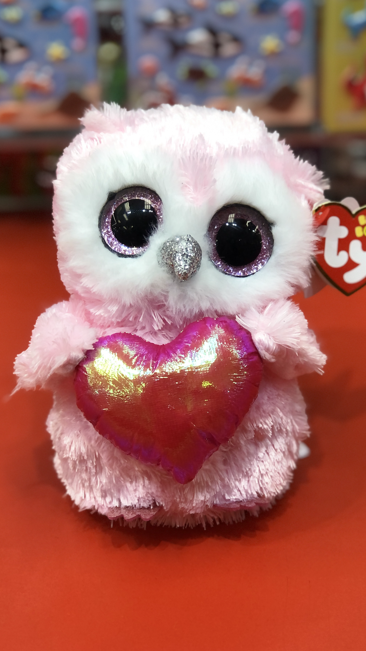 Ty pink and white owl plush holding a red heart on a red background.