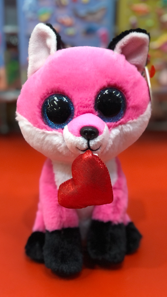 Ty pink fox plush with black ears and black feet with a red heart sitting on a red surface. 