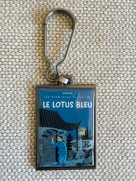 A rectangular keychain displaying the newly colorized book cover art for Hergé's Tintin adventure "Le Lotus Bleu." The atmospheric illustration shows Tintin wearing blue Chinese robes, hiding inside a large porcelain vase alongside Snowy, while a stylized black dragon looms on a vibrant red wall behind them in a dark Shanghai night scene.