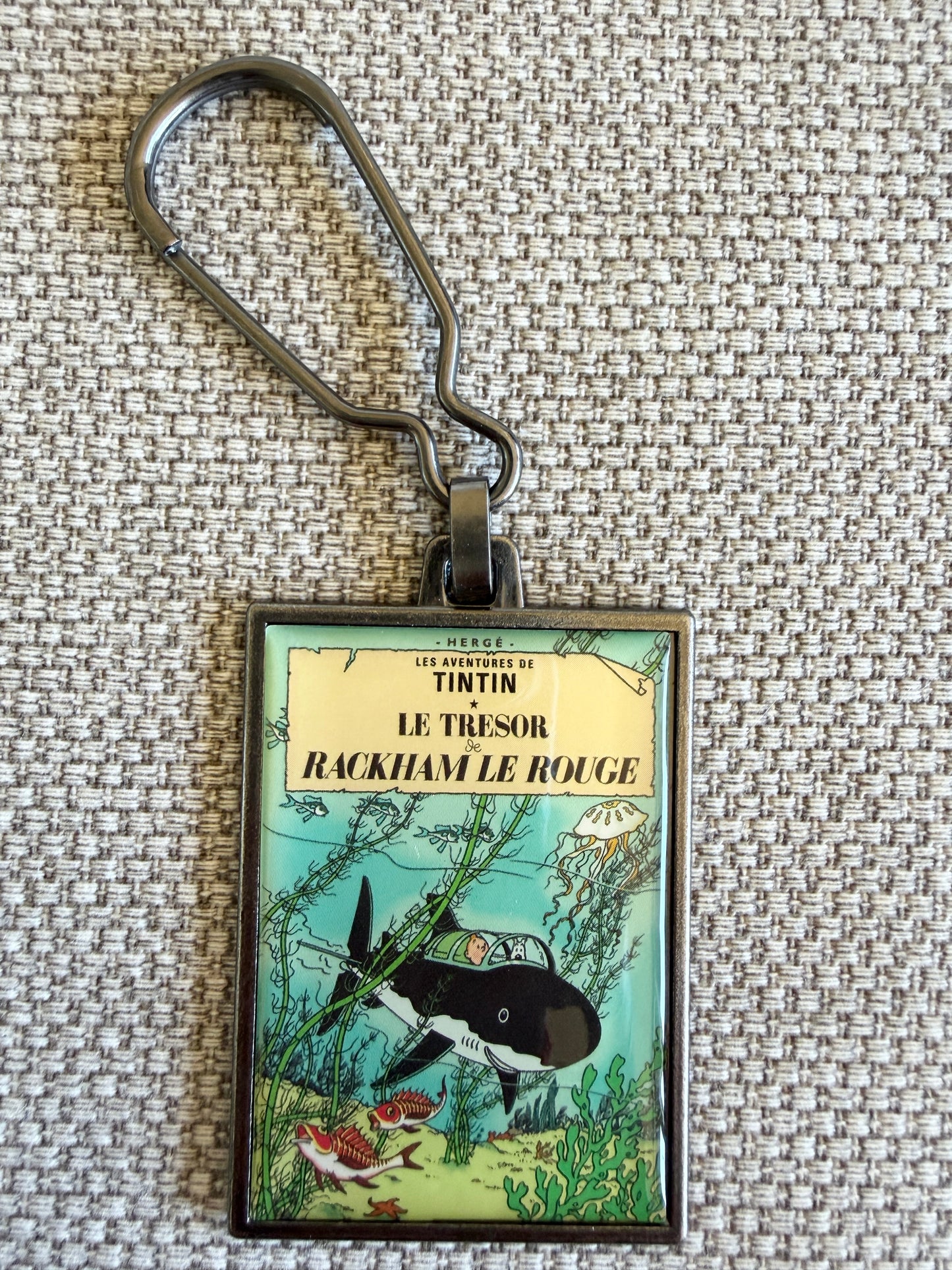 A close-up front view of an officially authorized, rectangular metal Tintin keyring. The crisp, resin-coated image reproduces the iconic cover of "Red Rackham's Treasure," showing Tintin and Snowy sitting together inside Professor Calculus's black shark-proof submarine as it navigates through vivid green underwater flora and small sea creatures on the ocean floor.
