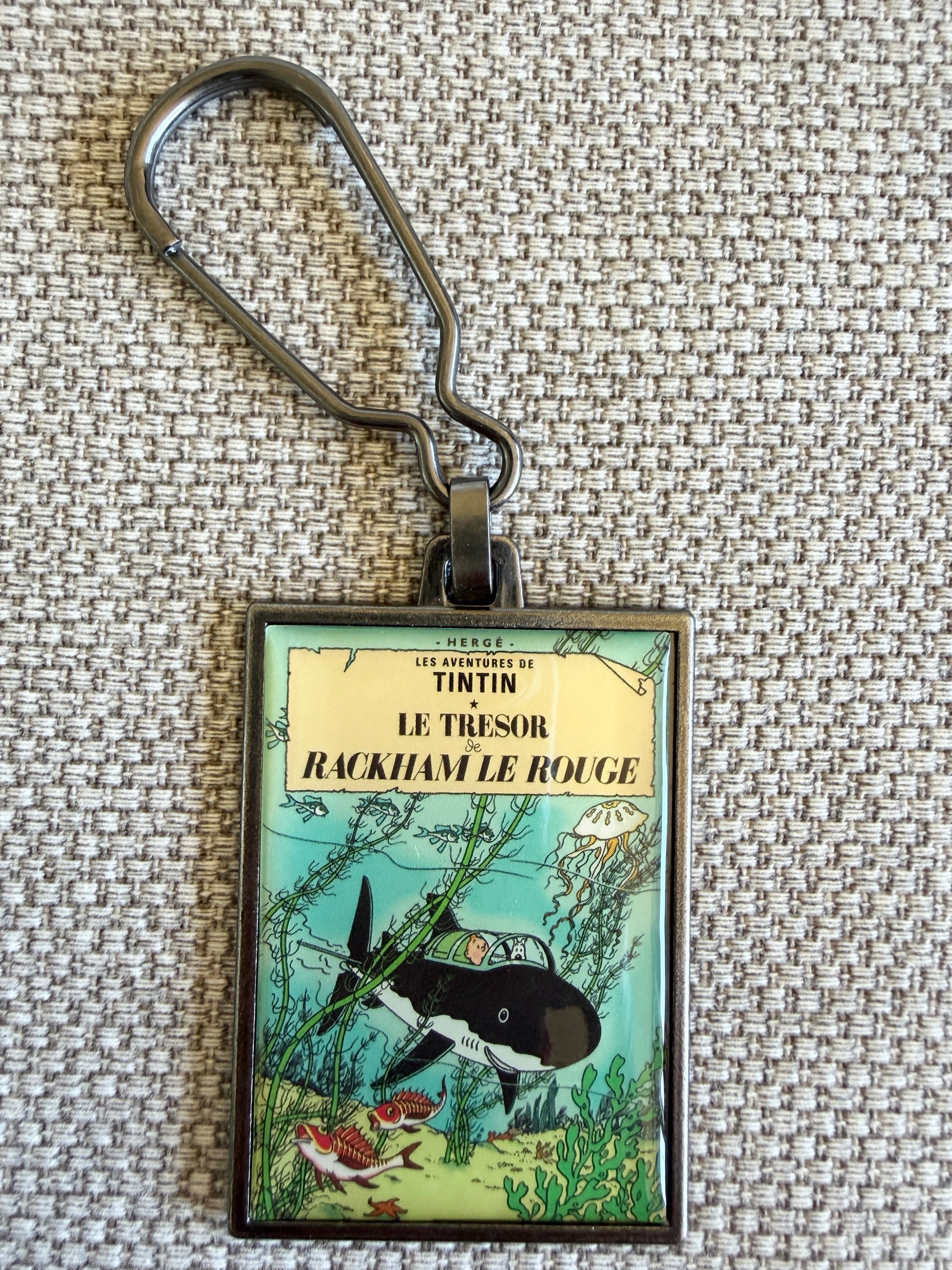 A close-up front view of an officially authorized, rectangular metal Tintin keyring. The crisp, resin-coated image reproduces the iconic cover of "Red Rackham's Treasure," showing Tintin and Snowy sitting together inside Professor Calculus's black shark-proof submarine as it navigates through vivid green underwater flora and small sea creatures on the ocean floor.