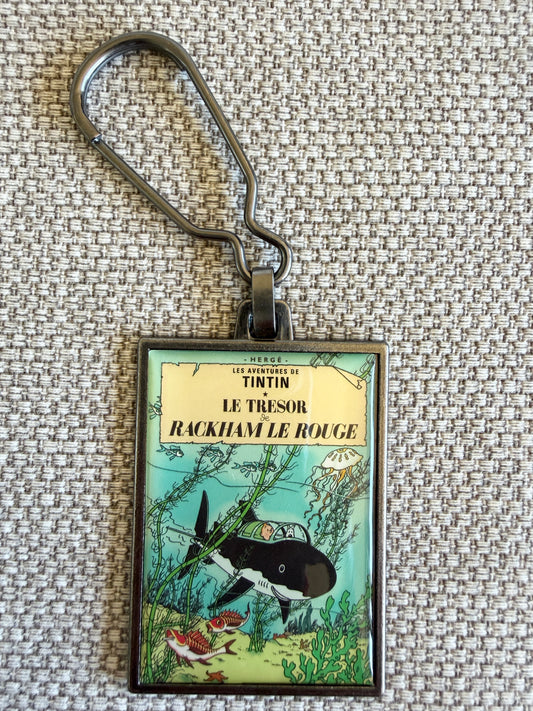 A close-up front view of an officially authorized, rectangular metal Tintin keyring. The crisp, resin-coated image reproduces the iconic cover of "Red Rackham's Treasure," showing Tintin and Snowy sitting together inside Professor Calculus's black shark-proof submarine as it navigates through vivid green underwater flora and small sea creatures on the ocean floor.