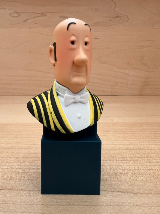 A mini PVC collectible bust figure of Nestor, Captain Haddock's loyal butler from Tintin, wearing a black and yellow striped waistcoat with a white bow tie, mounted on a dark blue square pedestal.