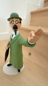 A GIF of a close-up, front three-quarter view of a 26cm resin collectible statue of Professor Calculus from Tintin. He is wearing his iconic long green coat, black round glasses, and a green bowler hat while looking forward, balancing a small black dowsing pendulum swinging back and forth from his extended left hand.