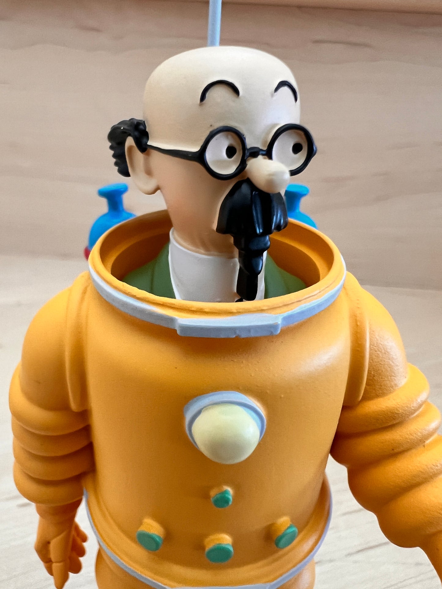 Close-up of a hand-painted Professor Calculus resin figurine wearing a bright orange moon cosmonaut suit with blue oxygen tanks, detailed with his iconic round glasses and black mustache.