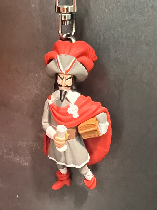 A mini plastic keychain figure of the pirate Red Rackham from Tintin, wearing a grey coat with a red cape and a large red-feathered tricorn hat, holding a golden goblet and a small wooden treasure chest.
