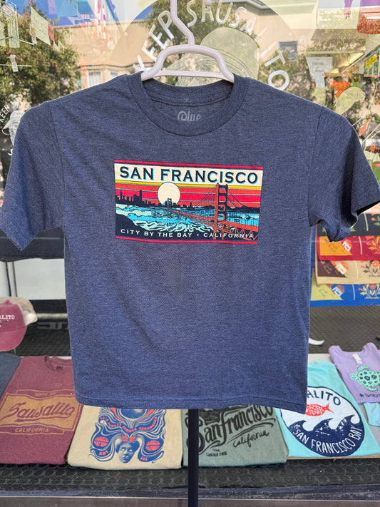 Blue t-shirt with San Francisco name drop against sunset design on a hanger photographed outside a storefront. 