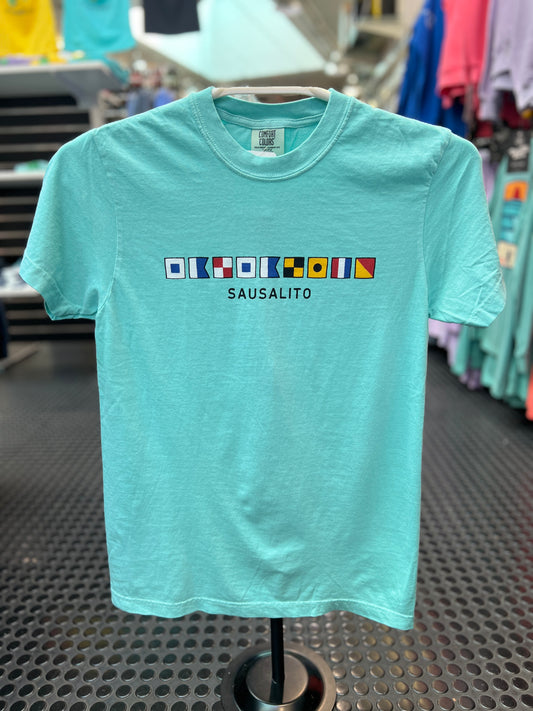 A Comfort Colors short sleeve t-shirt featuring a horizontal row of colorful maritime nautical signal flags that spell out 'Sausalito' across the chest."