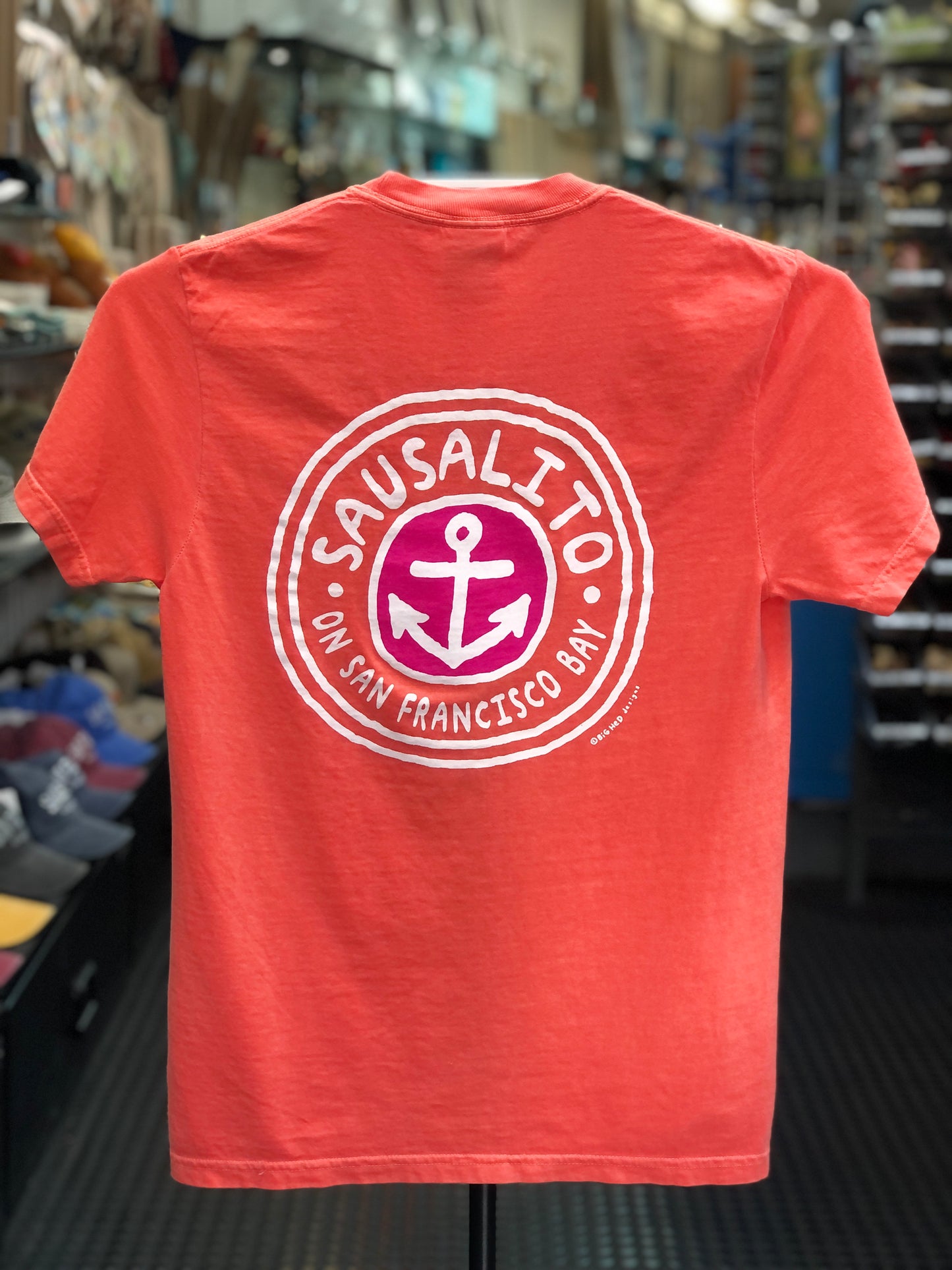 Bright Salmon orange Comfort Colors t-shirt featuring a circular "Sausalito On San Francisco Bay" anchor logo printed on the back, displayed on a clothing hanger.