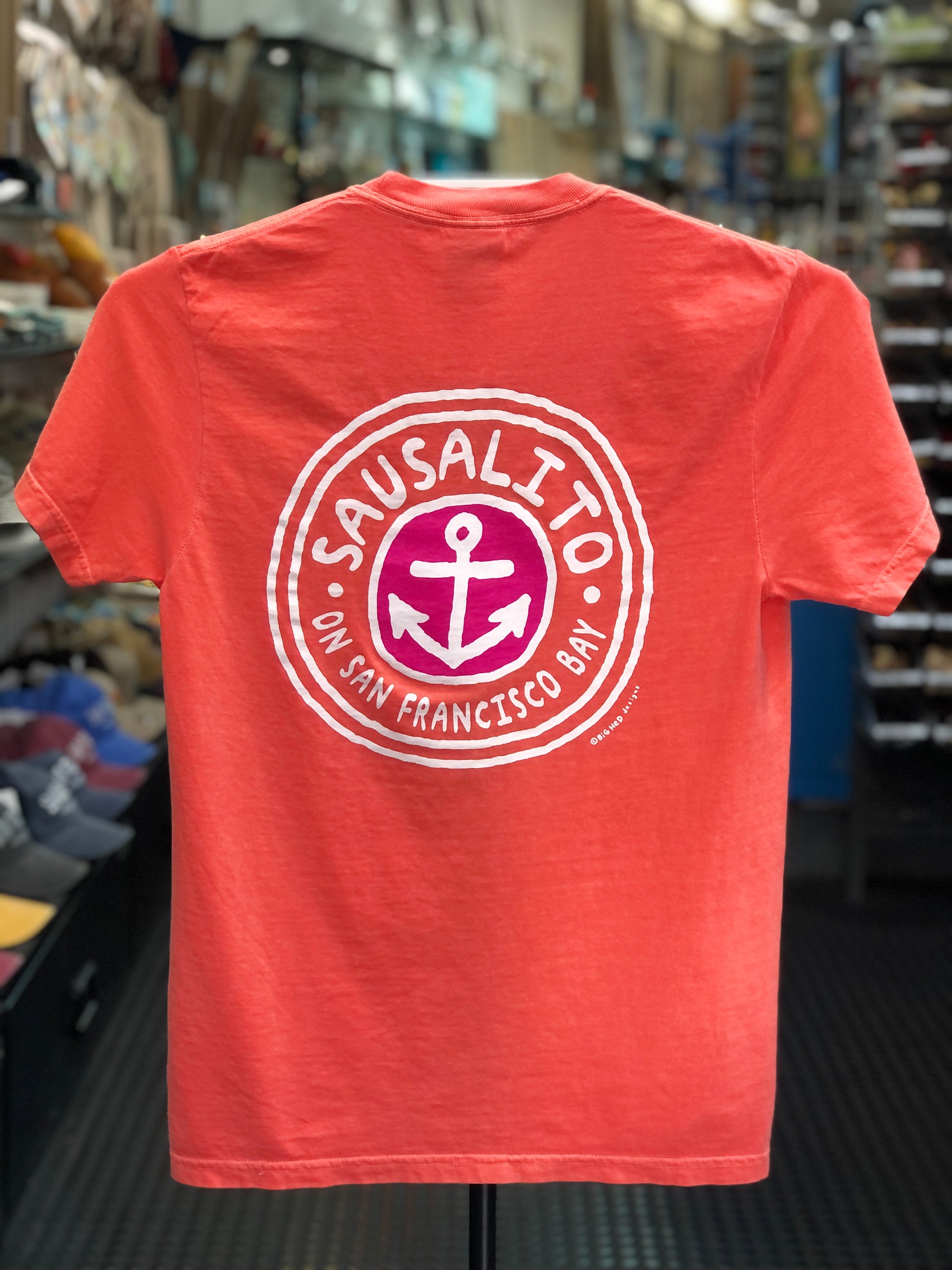 Bright Salmon orange Comfort Colors t-shirt featuring a circular "Sausalito On San Francisco Bay" anchor logo printed on the back, displayed on a clothing hanger.
