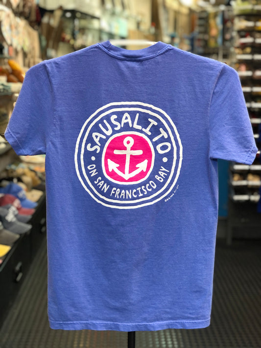 Blue Comfort Colors t-shirt with a circular logo featuring an anchor and text on a hanger in a store. 