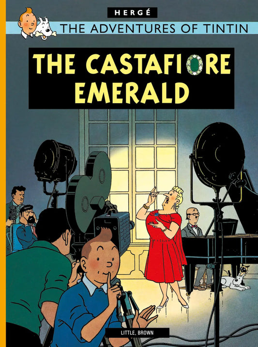 Comic book cover for The Castafiore Emerald. In the foreground, Tintin holds a finger to his lips in a "shush" gesture. In the background, the opera singer Bianca Castafiore is singing passionately on a stage with a pianist, under bright studio lights. Captain Haddock and other characters are visible in the wings, looking exhausted or annoyed.