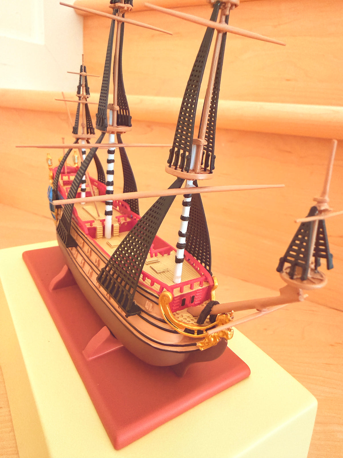 Detailed side-angle view of The Unicorn collectible model ship from The Adventures of Tintin, showcasing its intricate multi-tiered rigging, masts, and red hull displayed on a base.