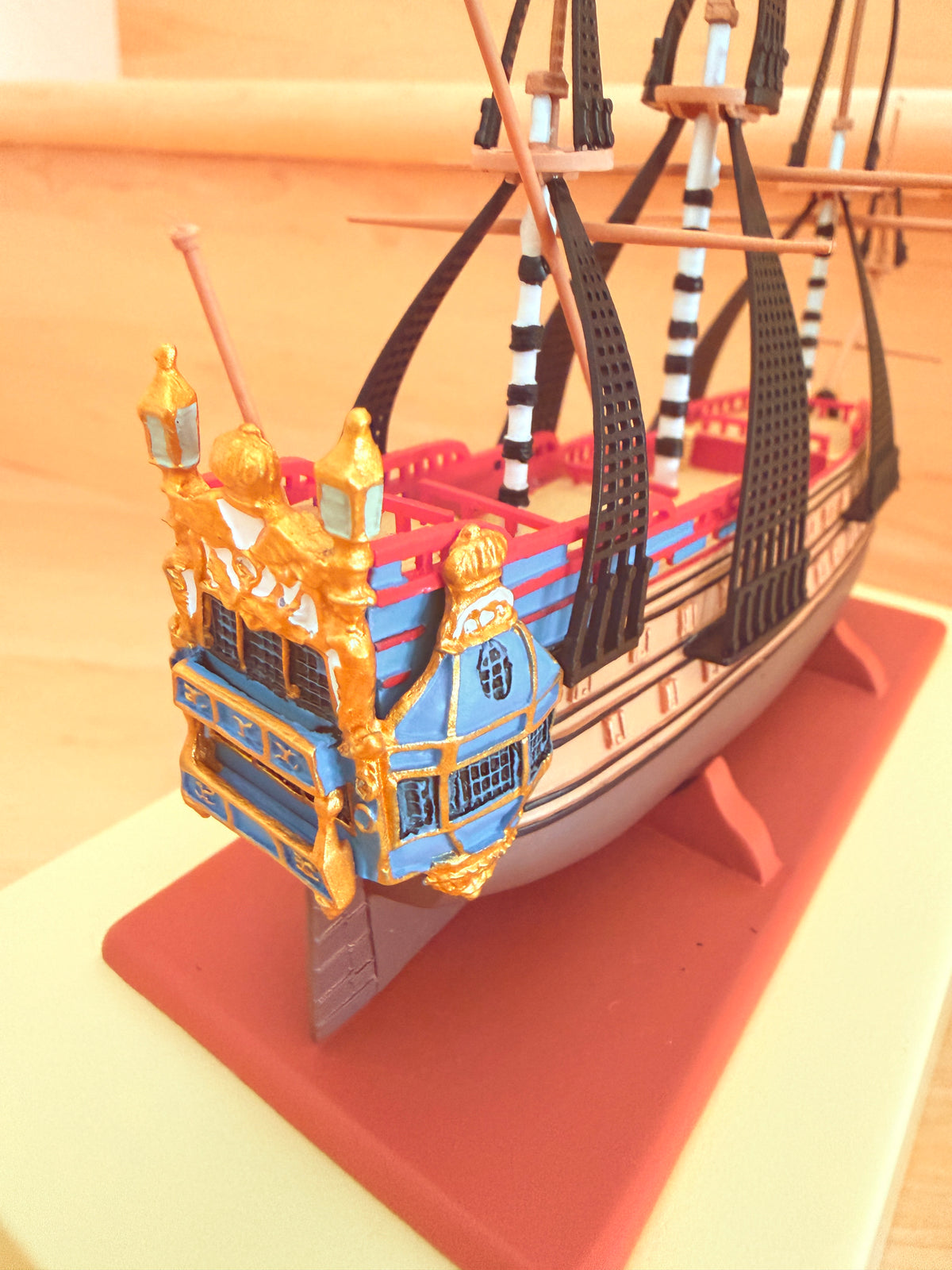 Close-up rear quarter view of The Unicorn collectible model ship from The Adventures of Tintin, showcasing its ornate blue and gold stern gallery, intricate rigging, and red display base.
