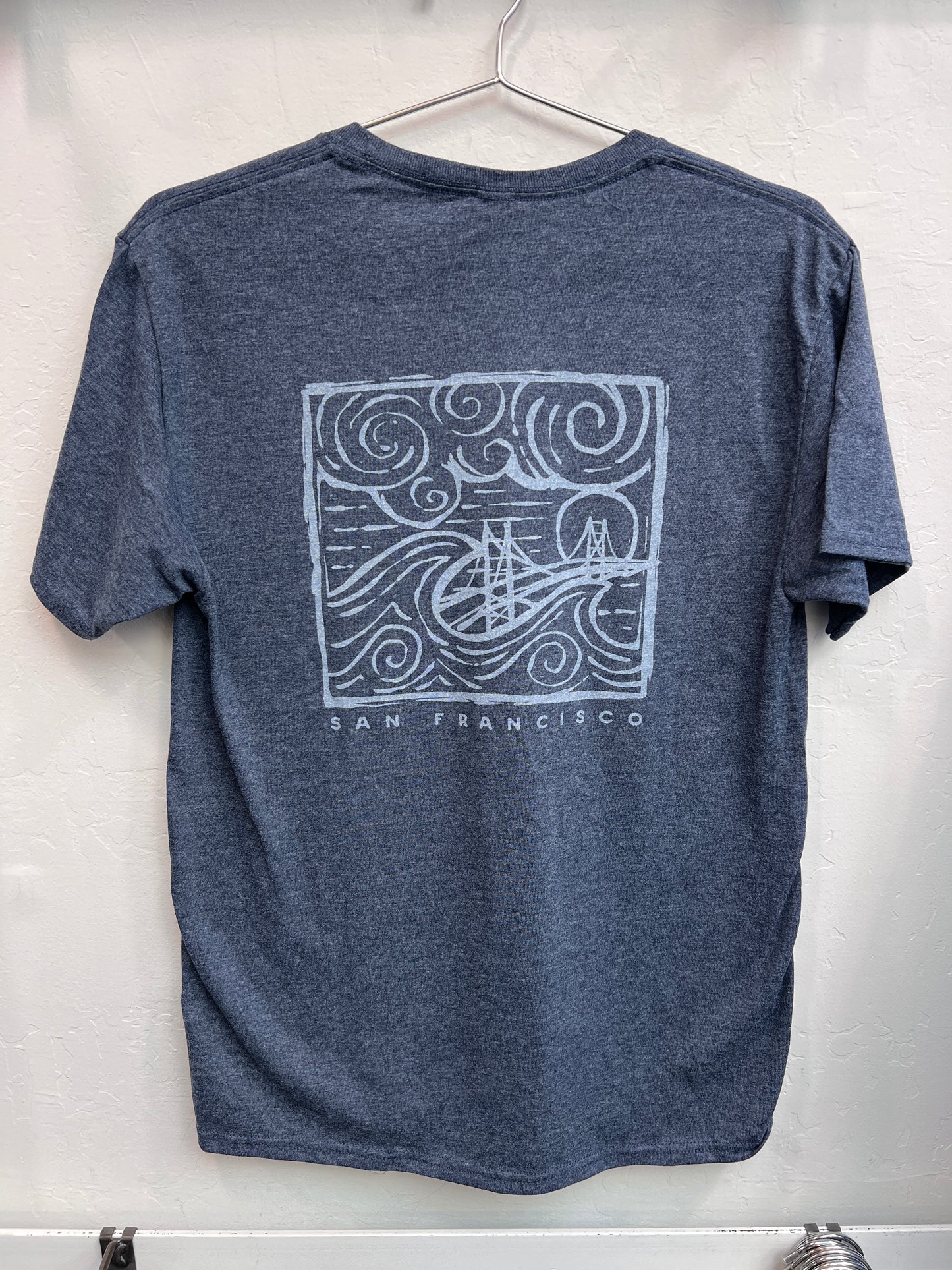 Retro Golden Gate Bridge design with swirling fog and waves printed on the back of a navy heather unisex t-shirt.