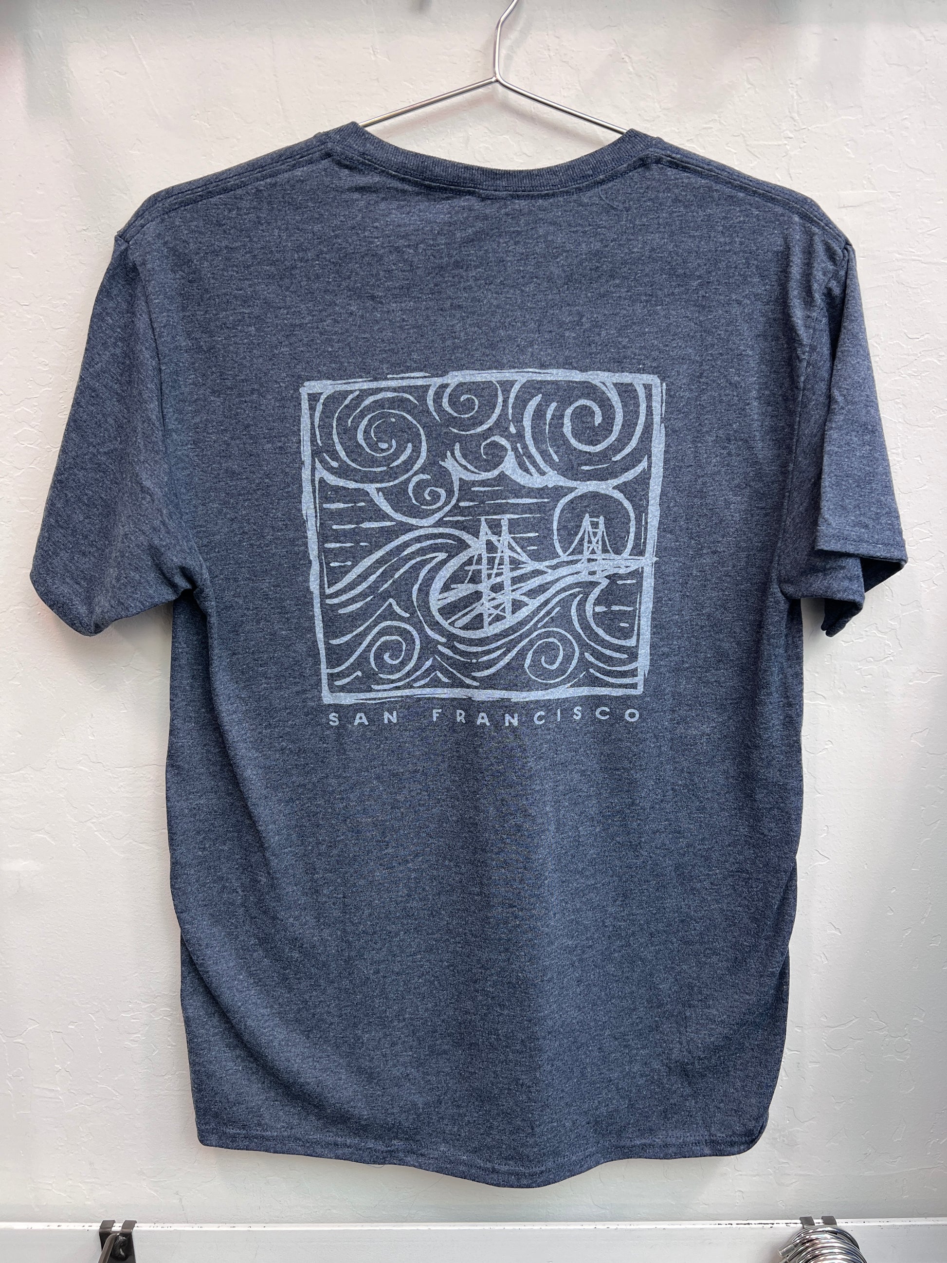 Retro Golden Gate Bridge design with swirling fog and waves printed on the back of a navy heather unisex t-shirt.