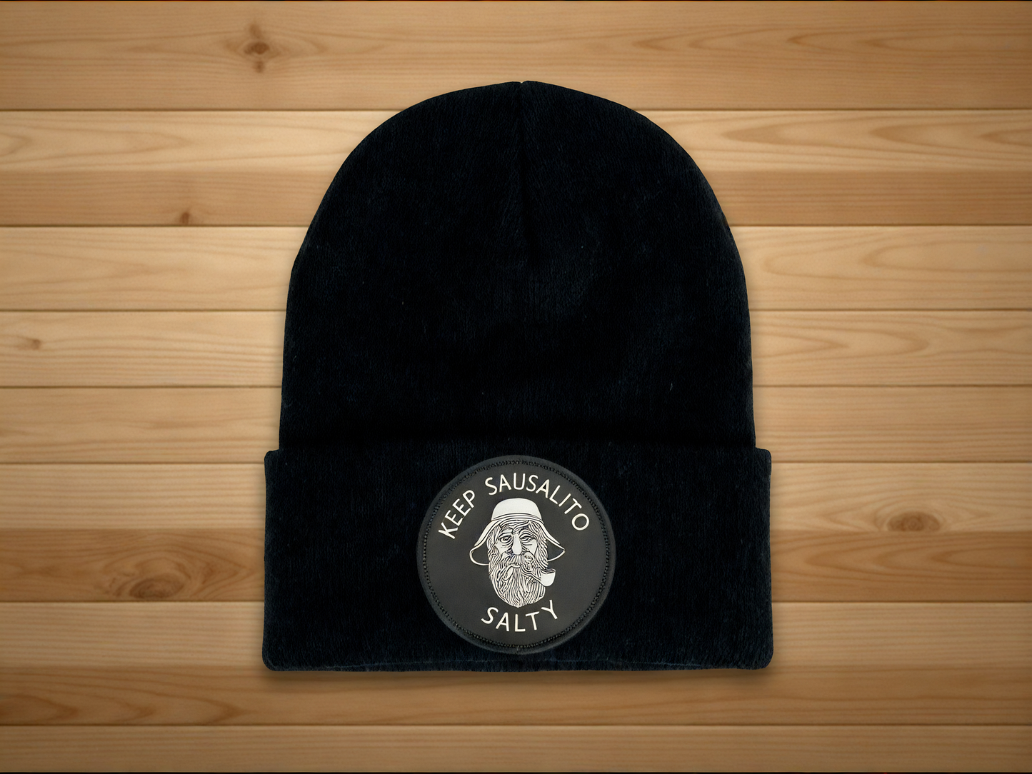 Black beanie with Keep Sausalito Salty patch on a wooden surface
