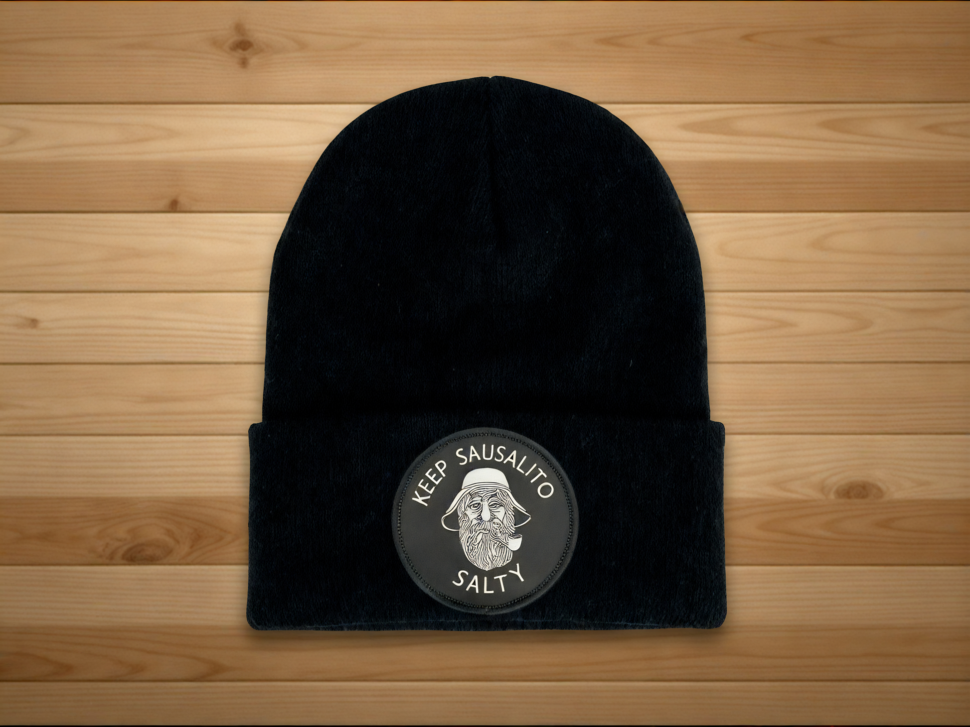 Black beanie with Keep Sausalito Salty patch on a wooden surface