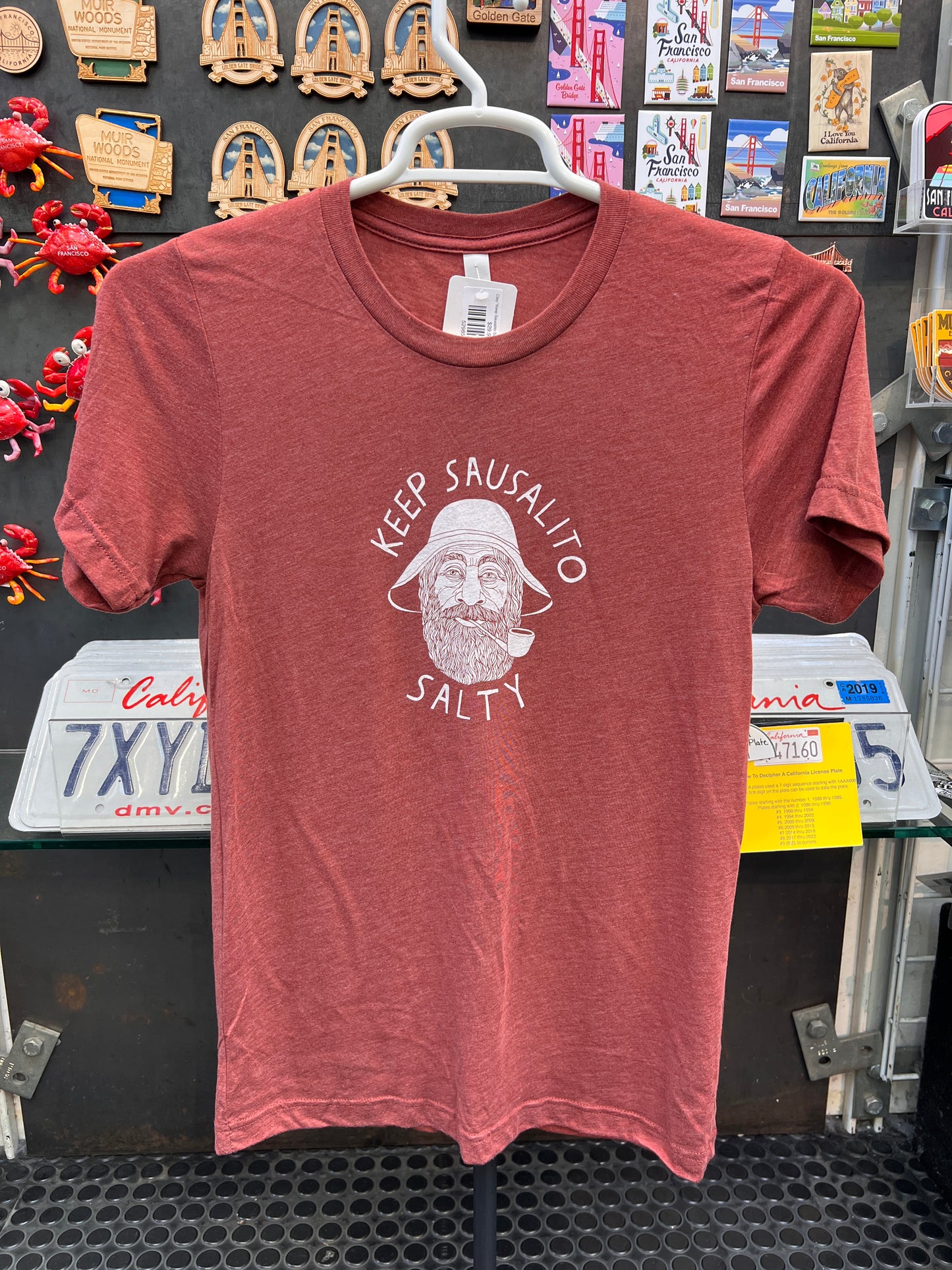 Clay Keep Sausalito Salty Unisex Short Sleeve T Shirt in a reddish-clay color featuring a white circular graphic of a bearded fisherman with "Keep Sausalito Salty" text.