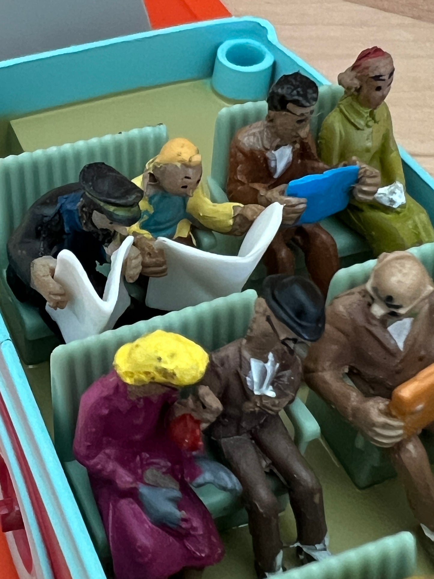 Close-up view of the interior of the 1/43 scale Swissair bus model from Tintin's The Calculus Affair, featuring hand-painted passenger figures including Tintin and Captain Haddock sitting in the back row reading newspapers.