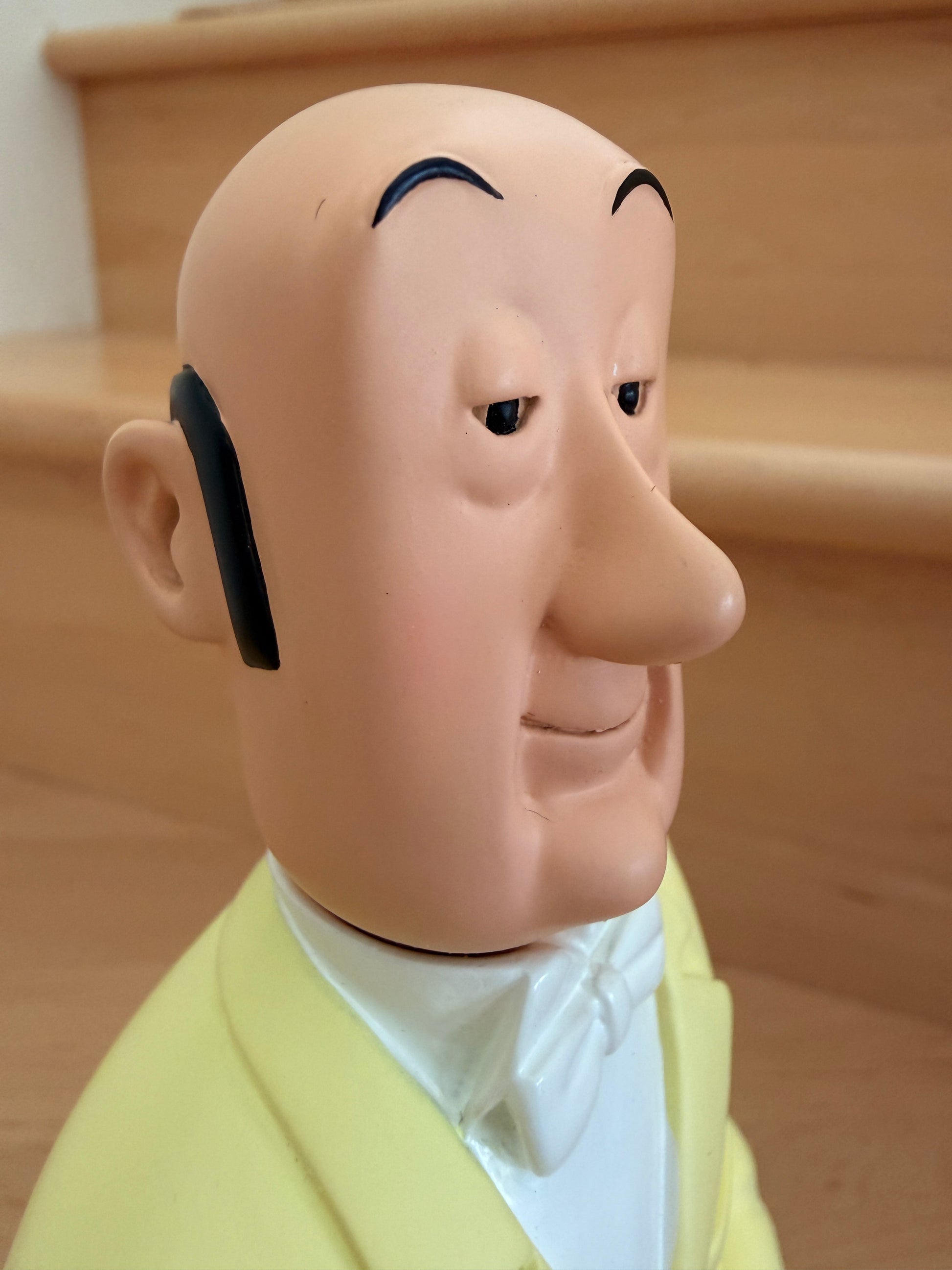 Close-up profile view of the Tintinimaginatio Icons collection Nestor resin figurine. The shot captures the butler from the chest up, focusing on his calm, stoic expression, arched black eyebrows, and distinctive profile. He is wearing his signature yellow double-breasted suit jacket over a crisp white shirt and a neatly tied white bowtie.
