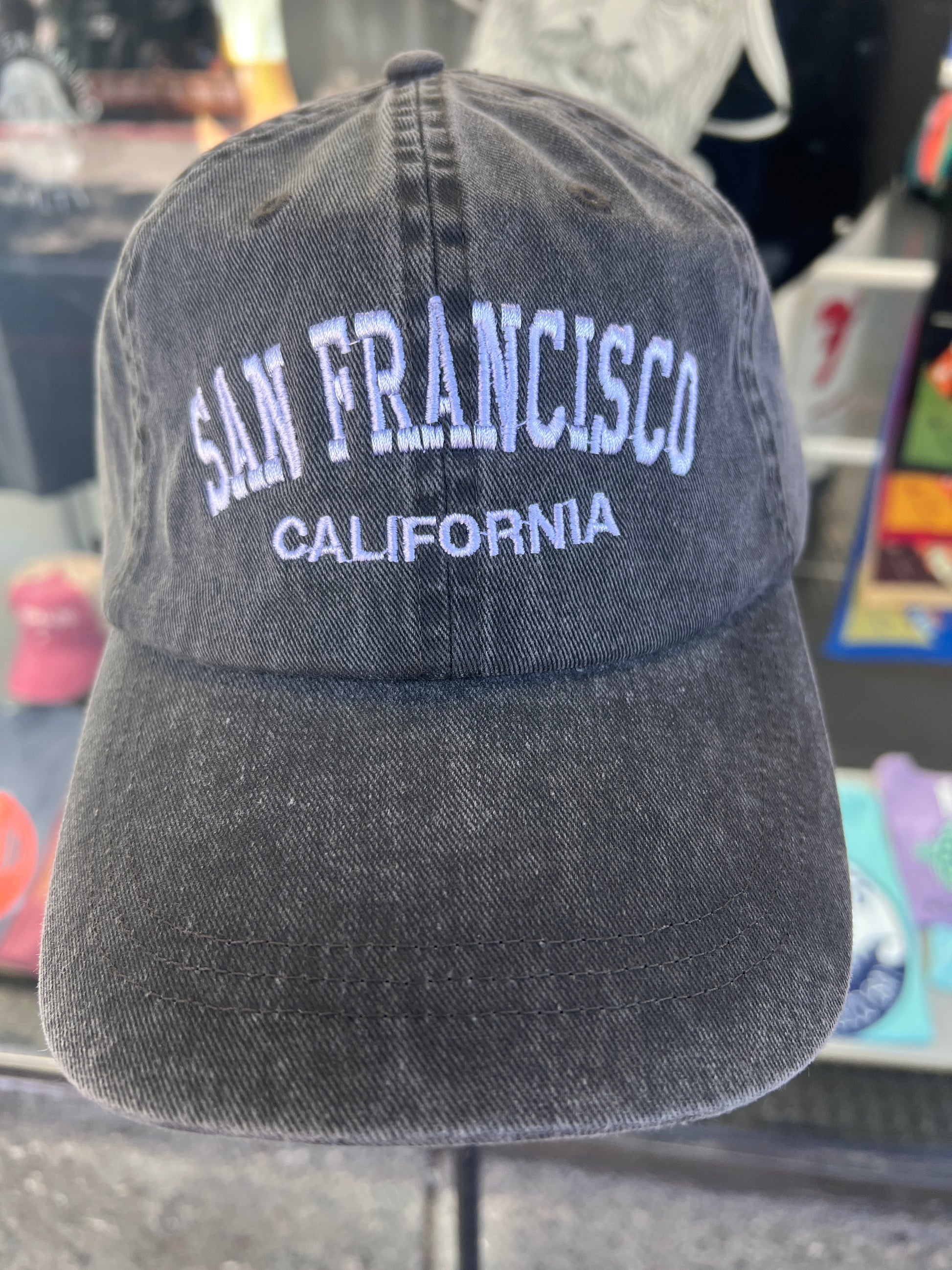 Front view of a charcoal grey washed cotton baseball cap featuring the words 'San Francisco' in a bold white arched font with 'California' embroidered directly underneath.