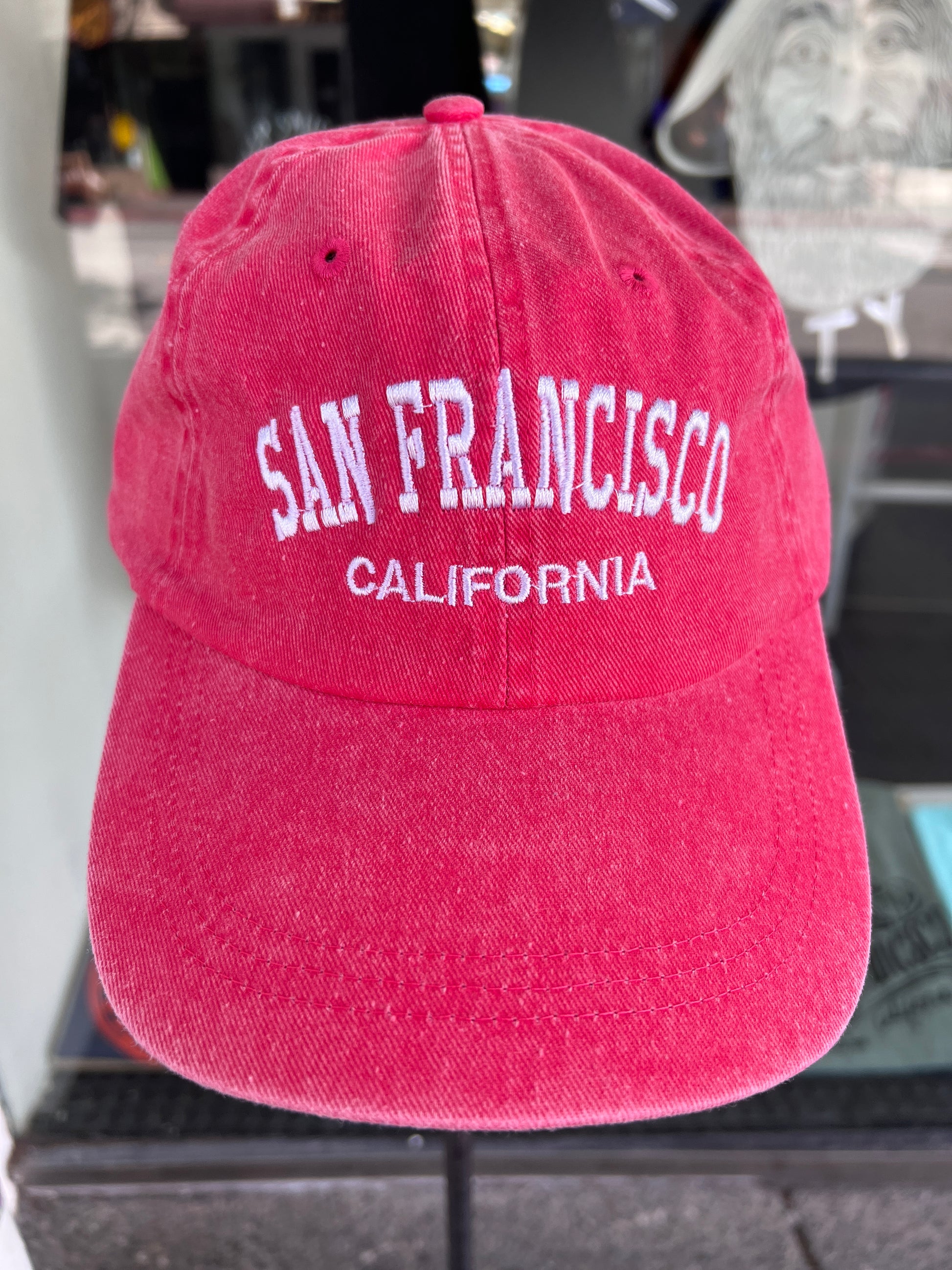 Front-facing view of a vibrant red washed cotton baseball cap featuring the words 'San Francisco' in a bold white arched font with 'California' embroidered underneath.